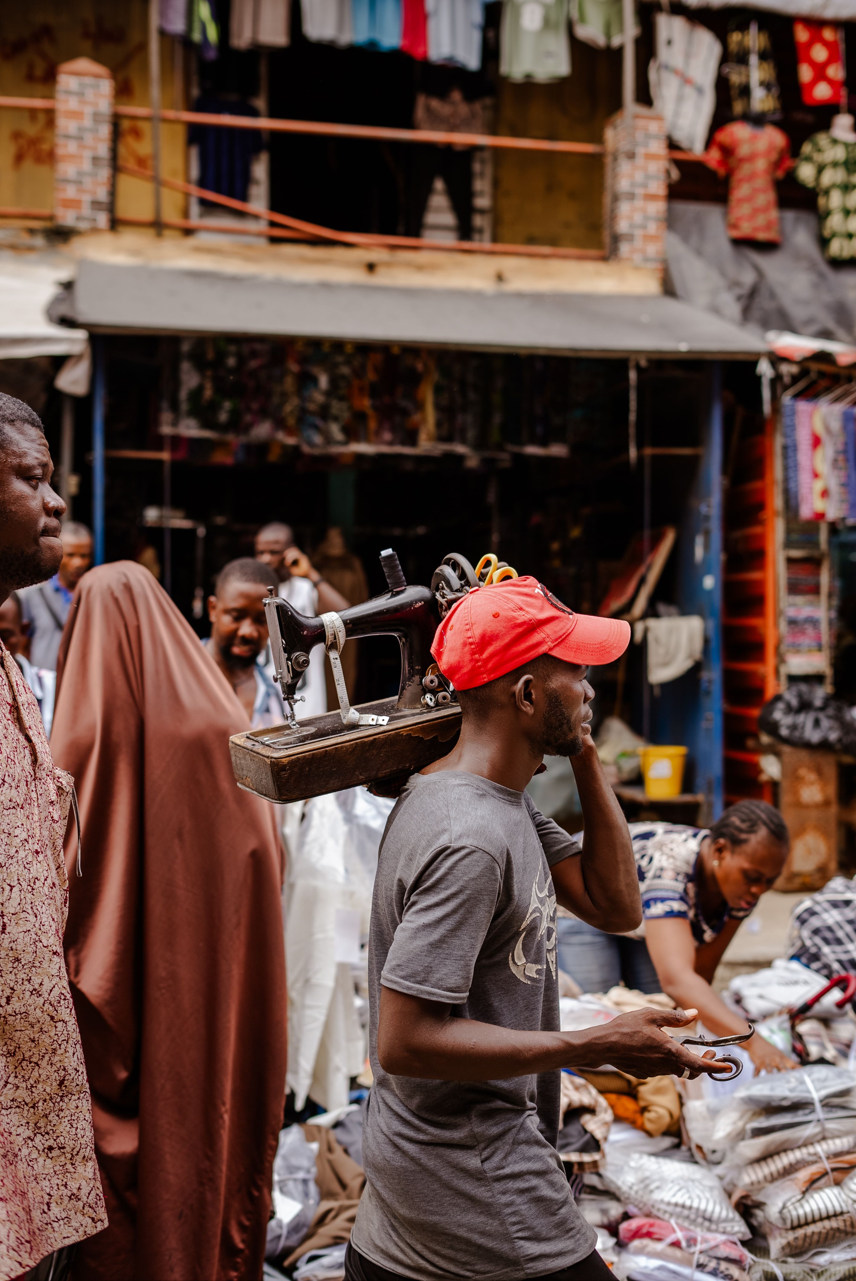 A tailor carrying a sewing machine through the market, representing an agent on their daily rounds